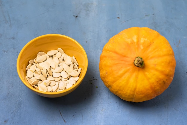 Foto ciotola gialla con semi di zucca salati su sfondo blu zucca cruda vista dall'alto