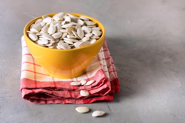 Yellow Bowl with Salted Pumpkin Seeds on Red Linen Napkin Gray Background Horizontal Copy Space