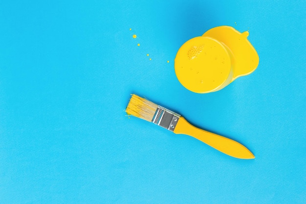 A yellow brush and a jar overflowing with yellow paint on a blue background Trending colors Minimal concept of interior selection Flat lay