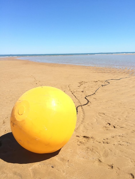 yellow buoy on beach against clear blue sky