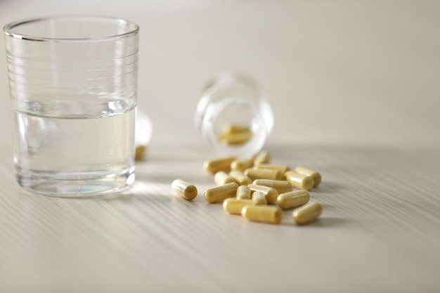 Yellow capsules spilled from pill bottle and glass of water on the table close up