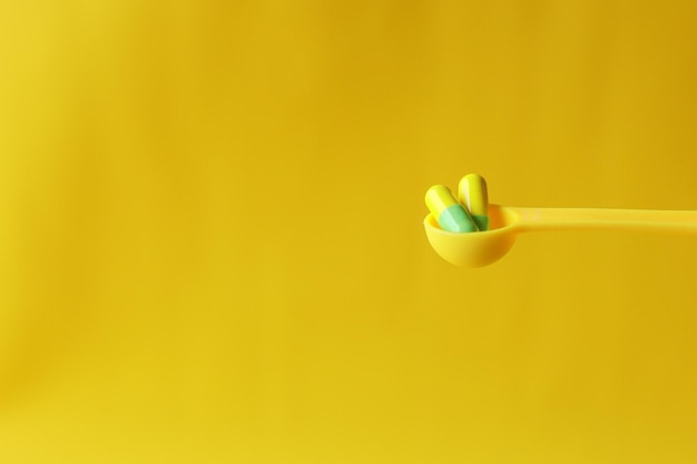 Yellow capsules on yellow fork isolated on yellow background with copy space Medical and pharmachy