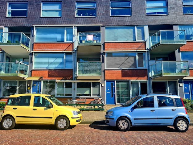 A yellow car is parked in front of a building with balconies.