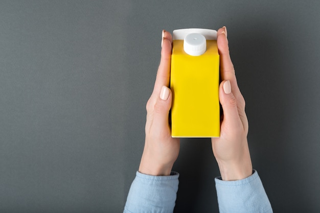 Yellow carton box or packaging of tetra pack with a cap in a female hands.  
