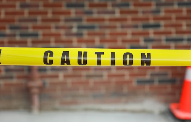 A yellow caution tape is taped to a brick wall.