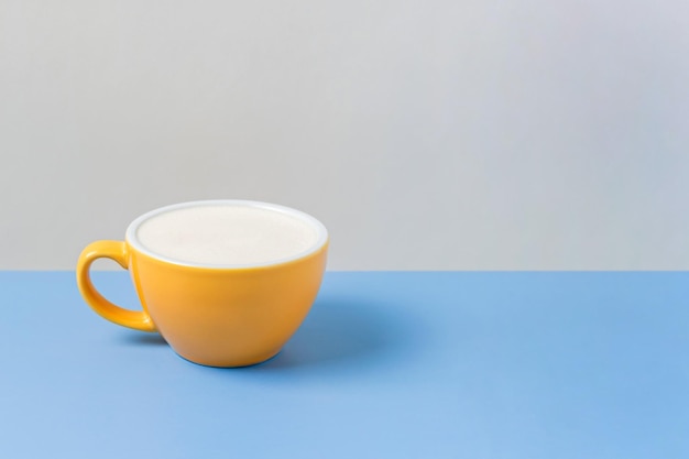 A yellow ceramic cup of coffee with steamed milk foam cappuccino latte on blue and beige background Horizontal image with copy space