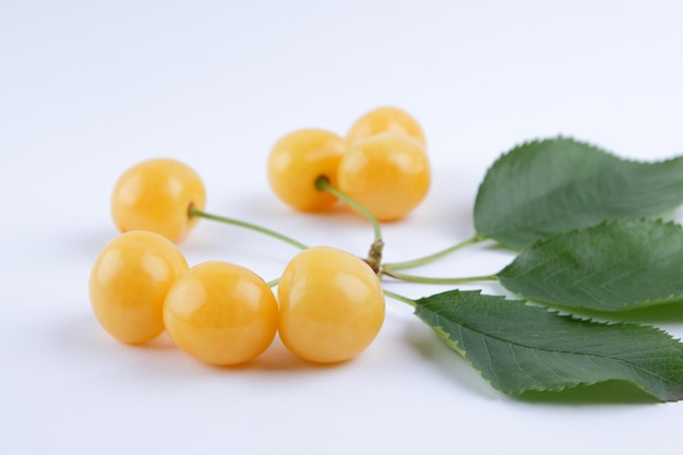 Yellow cherries on white background Fresh cherries with green leaves in minimalism style Copy space