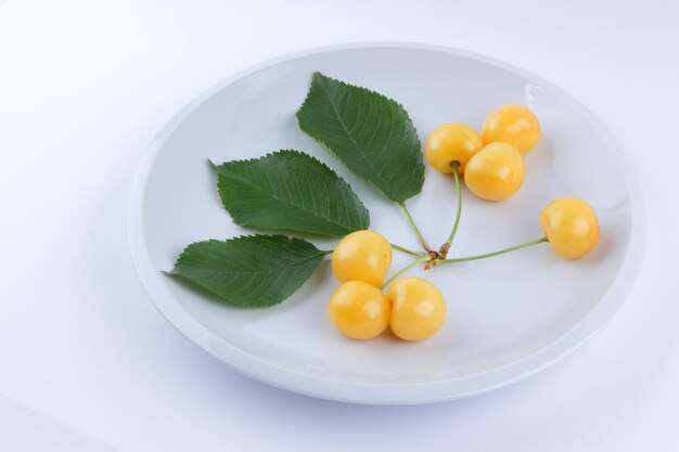 Yellow cherries with green leaves on white plate Fresh cherries on white background Close up