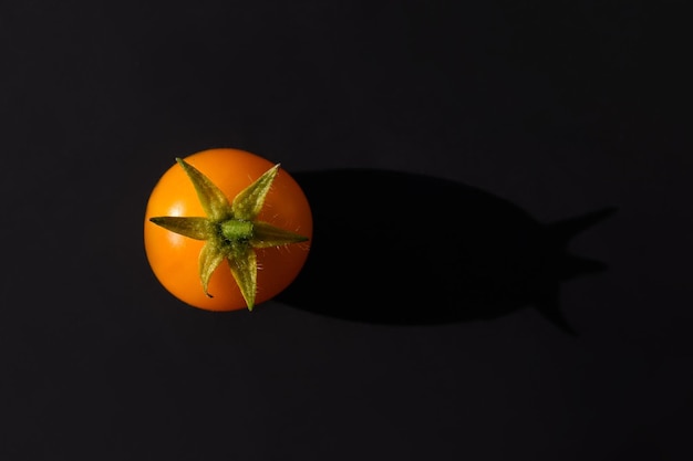 A yellow cherry tomato on a dark gray background with a black shadow. Close up, top view, copy space