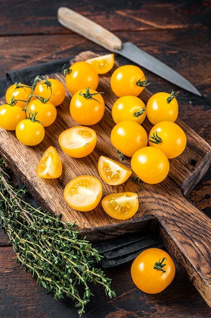 Yellow cherry tomato sliced on a wooden cutting board. Dark wooden background. Top view.