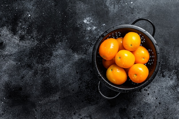 Yellow cherry tomatoes in a colander. Black background. Top view. Copy space.