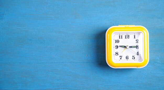 Yellow clock on blue wooden table.