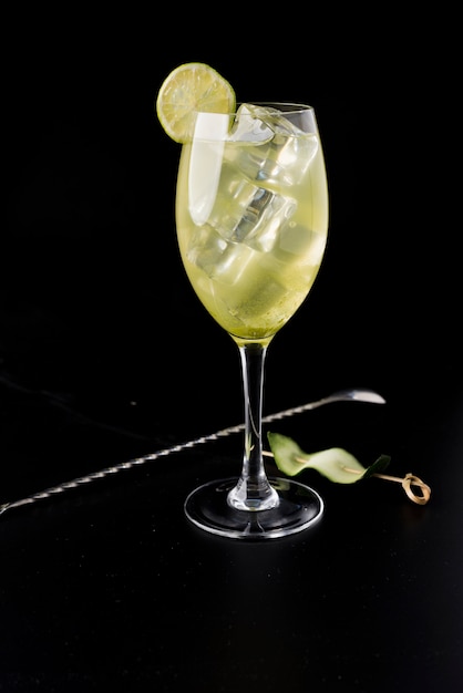 Yellow cocktail with ice, slice of lemon, cucumber skewer and spoon to remove