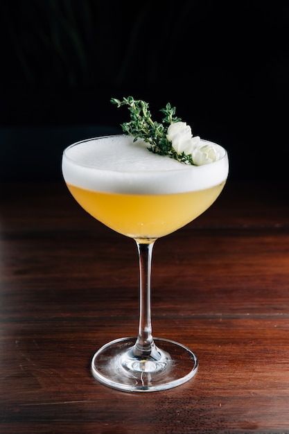 Yellow cocktail with white foam decorated with white flower and green branch. Studio Shot.