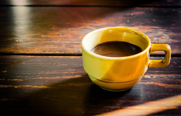 Foto tazza di caffè giallo sul vecchio tavolo in legno tra il sole