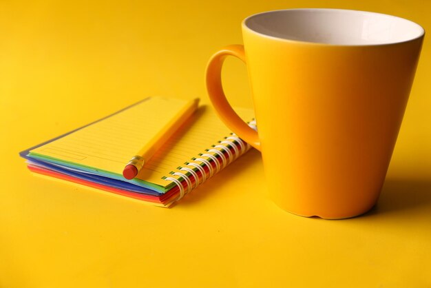 Yellow color notepad with pencil and coffee mug on yellow background