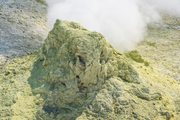 火山の斜面にある煙るソルファタラの周りの結晶化した硫黄の黄色い円錐形