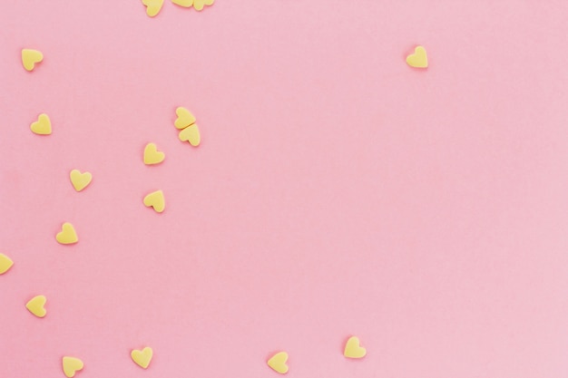 yellow confetti in the shape of hearts on a pink background copy space