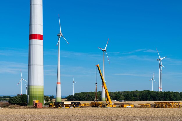 A yellow construction crane is assembling a metal structure in front of windmills