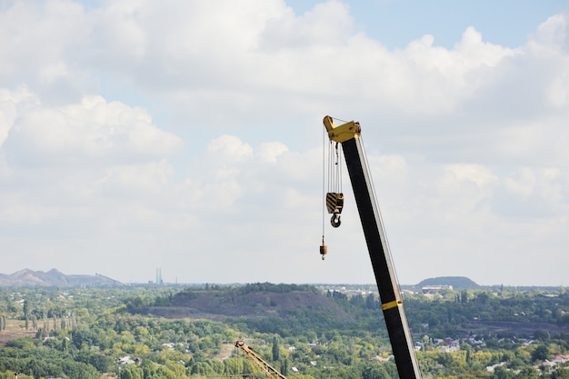 A yellow construction crane with hook against the sky