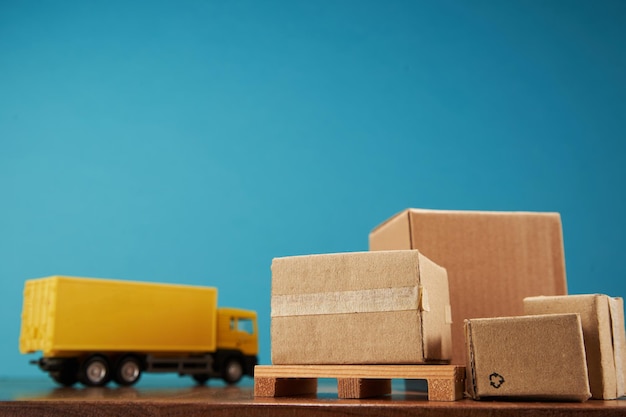 Yellow container truck with pallet of cardboard boxes against blue background