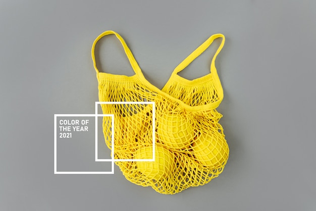 Yellow cotton net bag with lemons on grey background. colors of\
the year 2021 ultimate grey and illuminating. color trend palette.\
stylish background