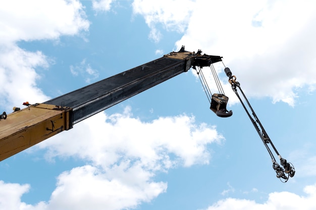 Yellow crane boom with hooks and blue sky background