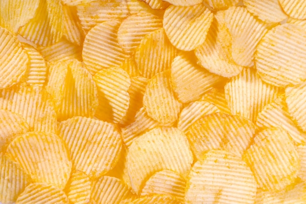 Yellow crispy ridged potato chips close up Food background