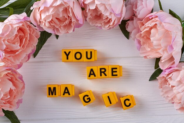 Yellow cubes arranged in you are magic words frame of peonies on white desk