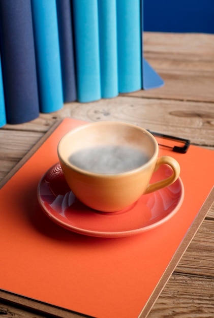 Yellow cup of coffee or tea with hot steam on note book with blue books and blue background