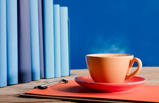 Tazza di caffè o tè gialla con vapore caldo sul taccuino con libri azzurri e sfondo blu