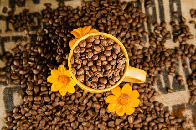 Foto tazza di caffè gialla con chicchi di caffè sul tavolo con uno sfondo naturale