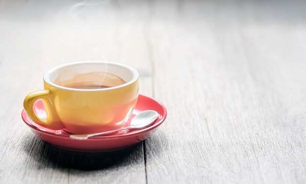 Photo yellow cup of coffee with red plate and spoon on wooden table, copy space.