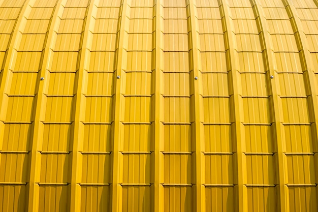 表面に日光が当たる黄色の湾曲した波形鋼屋根の背景