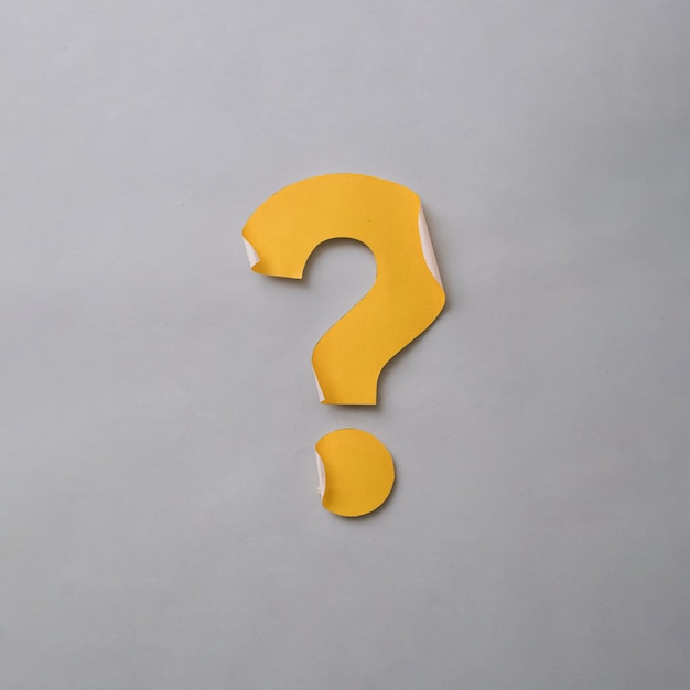 Yellow cut out question mark with curled edges over a grey card background in a conceptual image with copy space