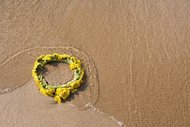 La ghirlanda di fiori di tarassaco giallo giace sulla spiaggia è bagnata dalle onde del mar baltico ligo l