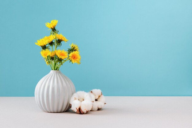 Yellow dandelions in vase on cian background close up copy space Bouquet sunny wildflowers dandelions in ceramic vase in bright background Artistic colorful spring or summer flower background