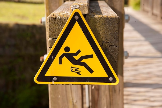 Yellow danger of slipping sign triangle on a wooden bridge