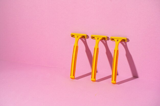 Yellow disposable razors on pink background, studio shot, copy space