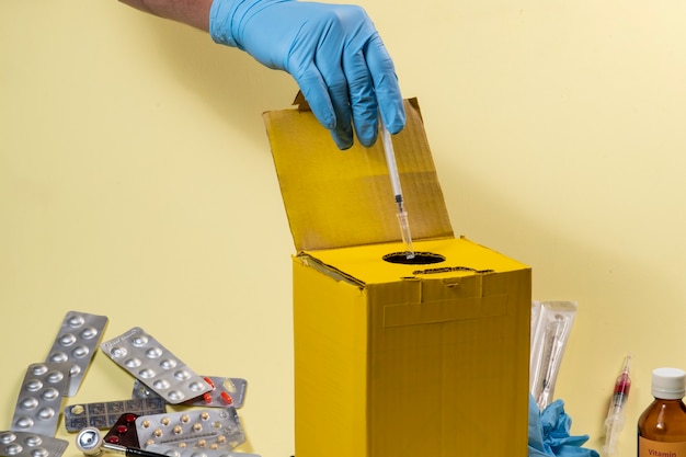 Yellow disposal box for contaminated or infectious products in a hospital or home. Hand putting a syringe