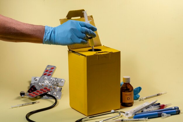 Yellow disposal box for contaminated or infectious products in a hospital or home. Hand putting a syringe