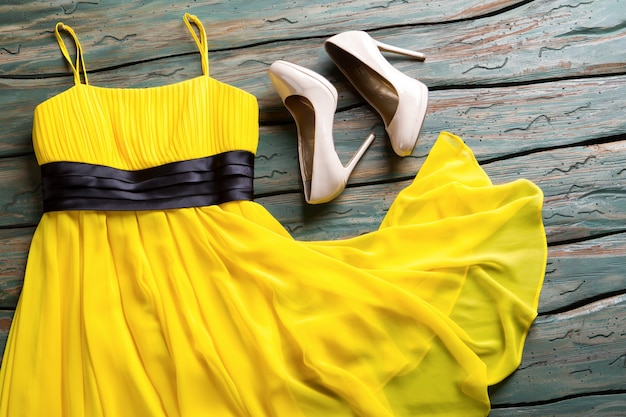 Желтое платье и бежевые каблуки. Глянцевые каблуки светлого цвета. Одежда на зеленом деревянном фоне. Простой вечерний наряд девушки.
