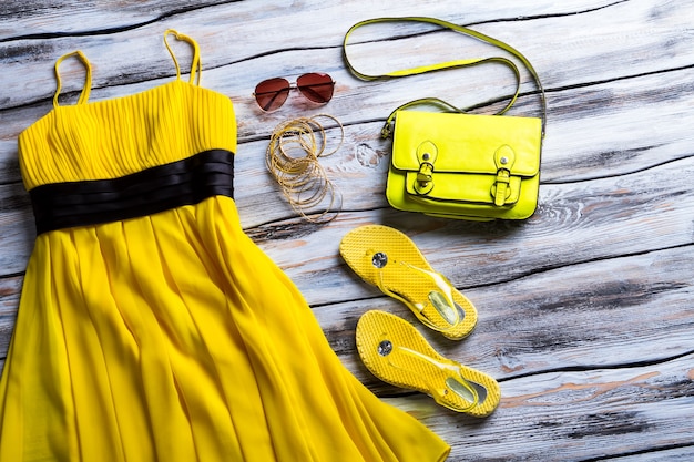 노란 드레스와 라임 핸드백. 선글라스와 팔찌로 옷을 입으십시오. 흰색 테이블에 여자의 의류입니다. 여름 의류의 저렴한 가격.