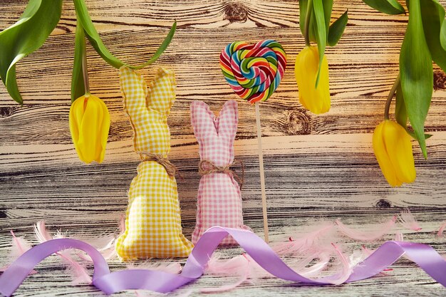 Yellow Easter background with handmade bunnies yellow tulips lollipop in shape of heart pink fluffy feathers Creative colorful spring Easter background