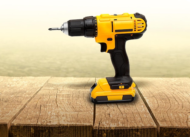 Yellow electric cordless screwdriver drill on wooden background professional home repair tool