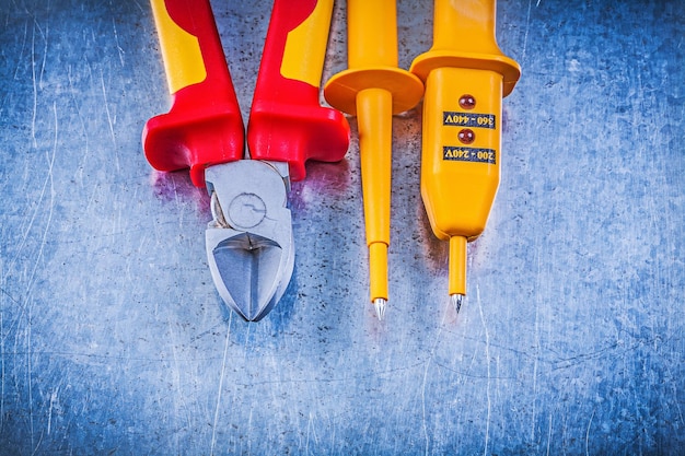 Yellow electrical tester red sharp cutting pliers on metallic background electricity concept