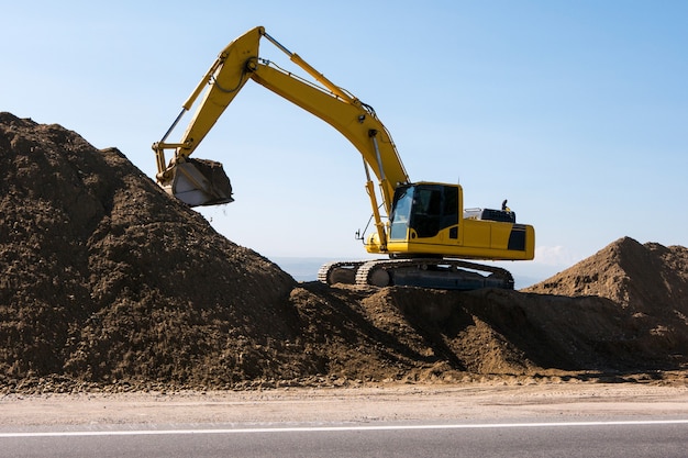 Yellow excavator loader machine during earthmoving works on blue sky. Construction machinery loading lifting on job sites