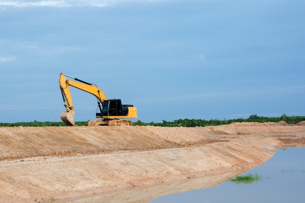 Yellow excavator machine working earth moving works riverside at construction site