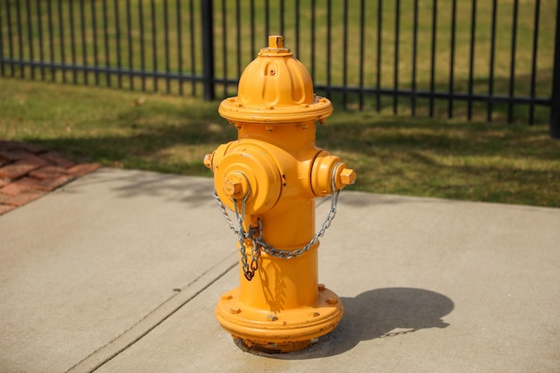 A yellow fire hydrant is on a sidewalk in front of a fence.