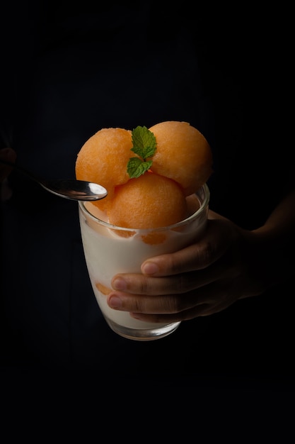 Photo yellow flesh melon was scooped into a round ball like ice cream put into a clear glass topped with fresh milk, sweet and delicious. take a picture on a black background